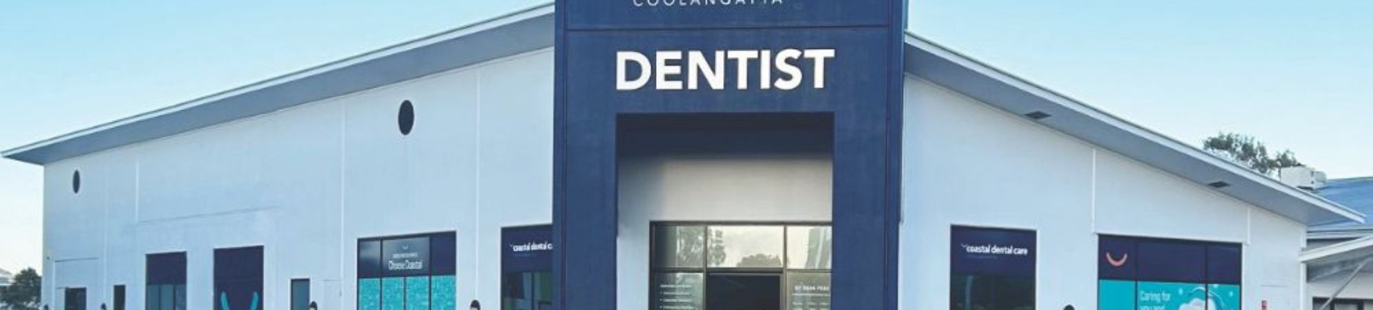 Store front of Coastal Dental Care, Dentist. A white building with dark blue features.